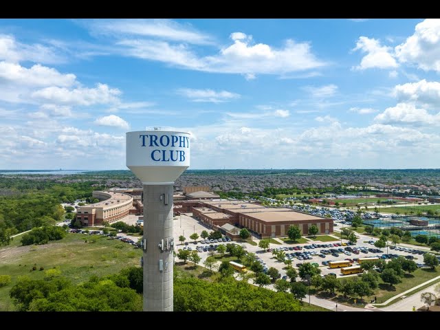 The Trophy Club water tower rising above school buildings, parking lots, sports courts, and neighborhoods on a clear day