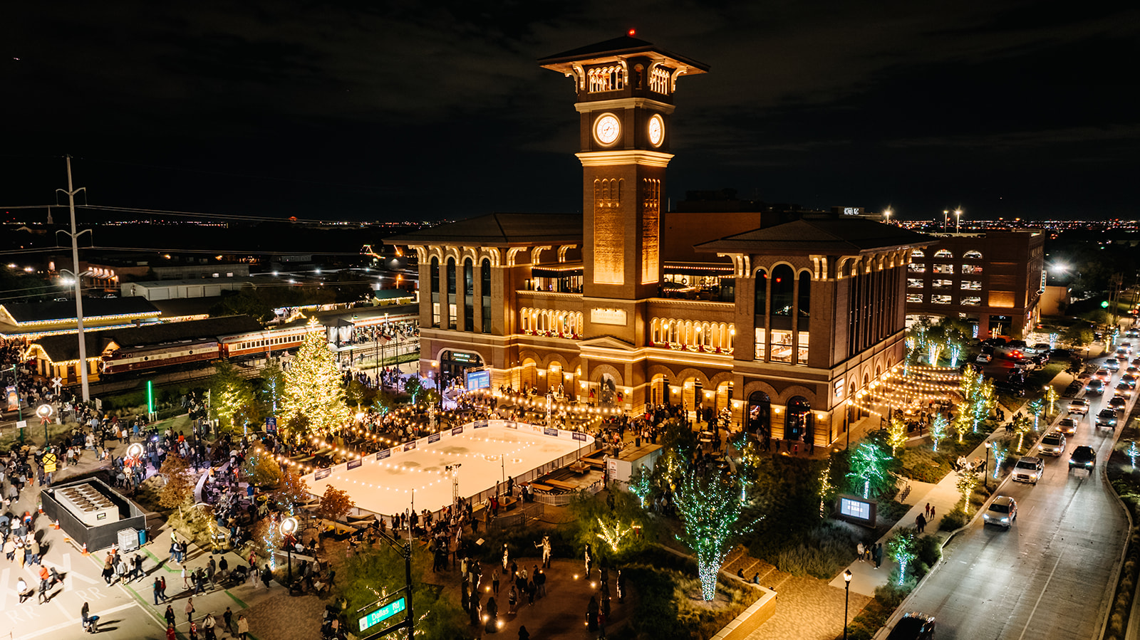 Grapevine Main Station and clock tower illuminated at night with a Christmas tree, train, and outdoor gathering spaces
