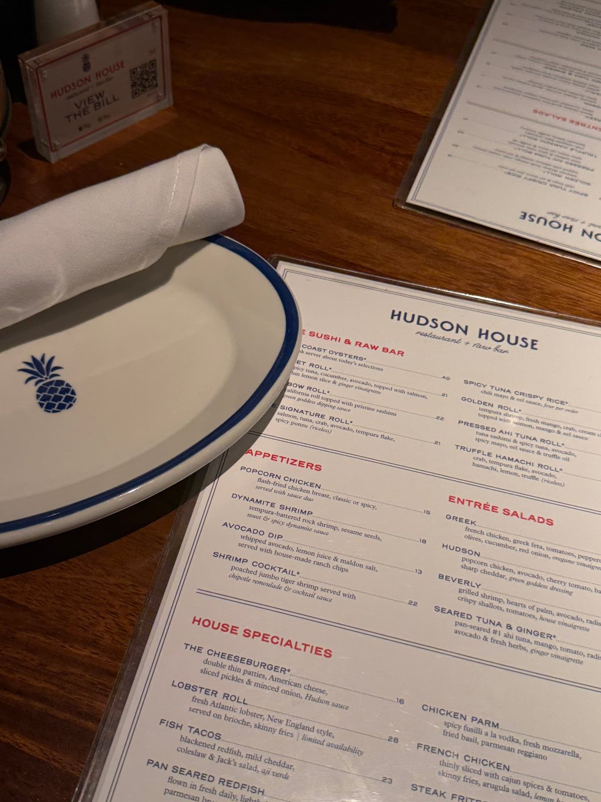 Hudson House menu listing sushi, raw bar, appetizers, and house specialties beside a blue-rimmed plate