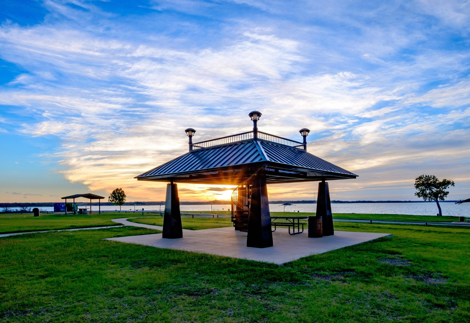 Lakeside picnic pavilion at Grapevine Lake framed by grass, water, and a blue evening sky