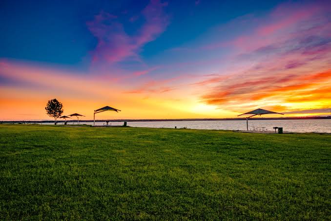 Sunset over Grapevine Lake with a green lakeside lawn and picnic shelters