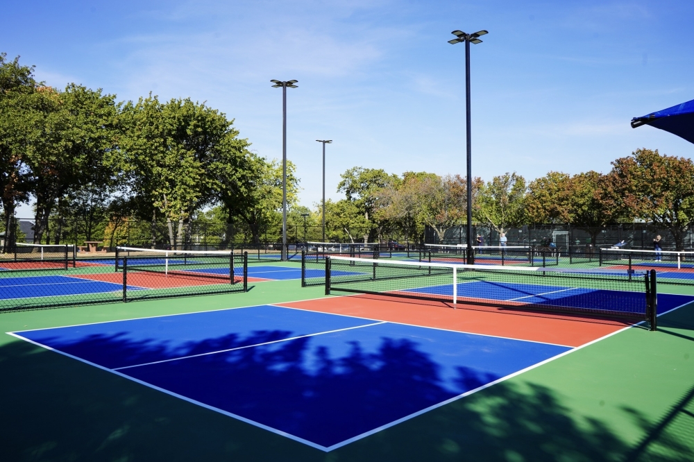 Pickleball courts in blue, red, and green at Harmony Park, framed by mature trees and light poles on a sunny day